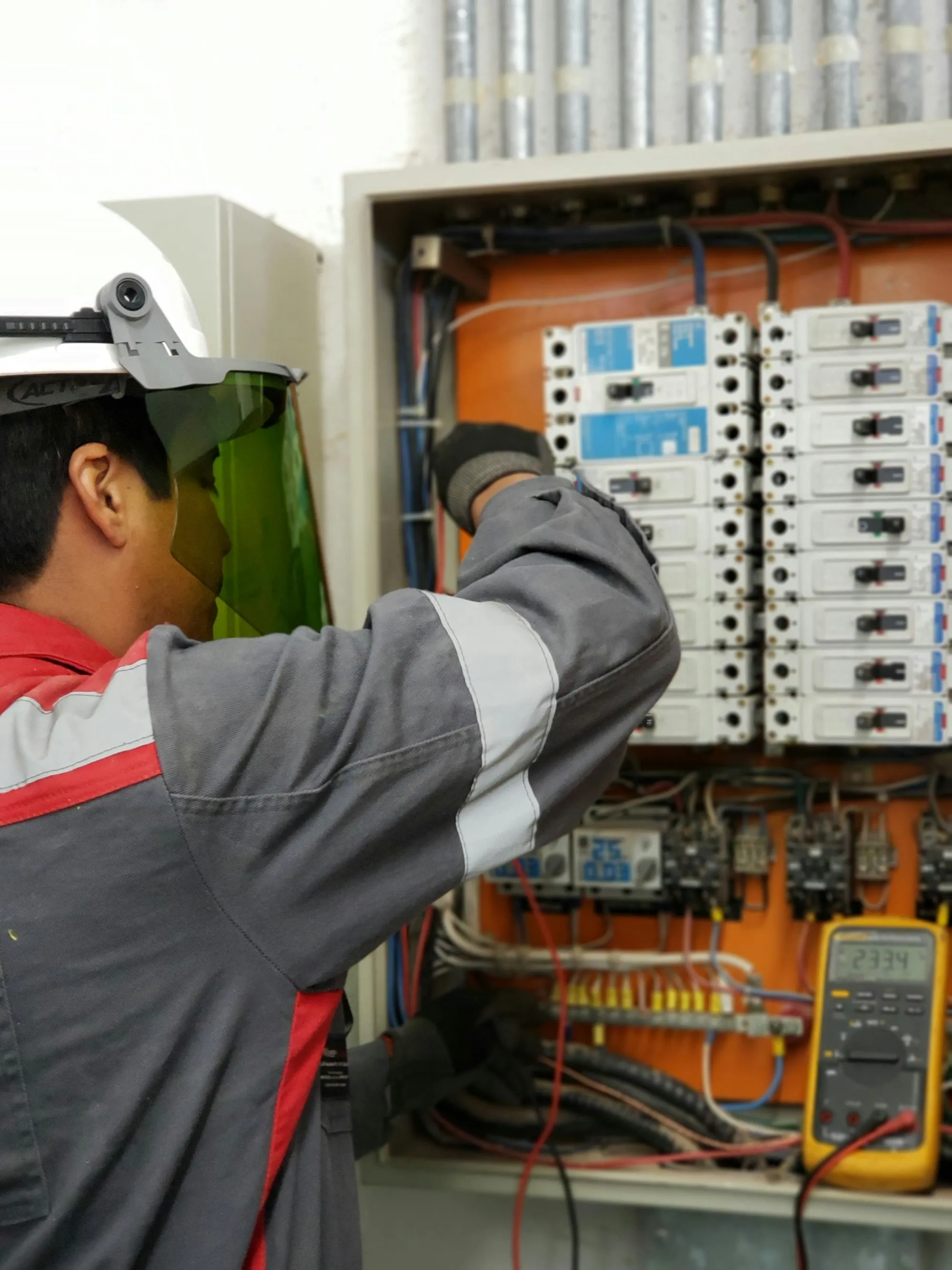 Engineer in a hard hat and face shield testing an electrical panel