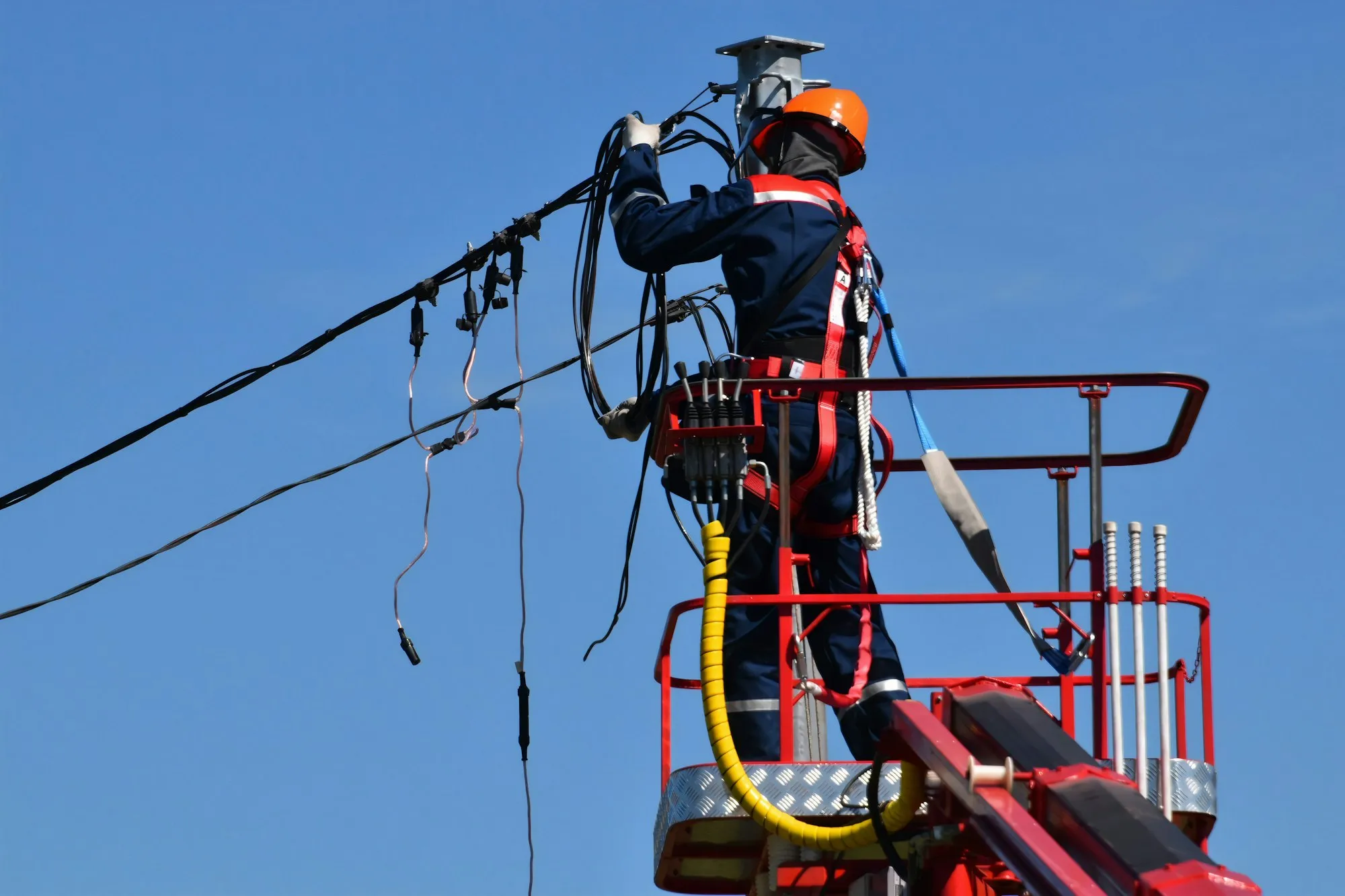 Line worker in a hard hat and harness connecting overhead power lines